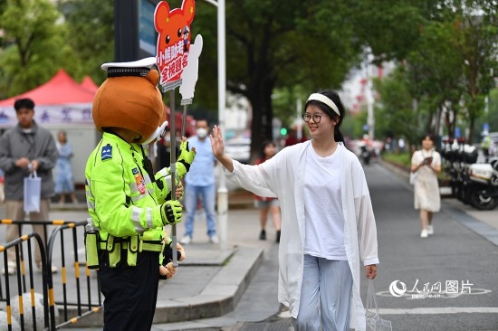 6月7日上午9時，隨著鈴聲的響起，2023年江西高考正式開考，江西省的53.57萬考生以縣（區(qū)）為單位隨機(jī)安排在全省256個考點、18968個考場參加高考。圖為“小熊交警”和考生擊掌鼓勵。 人民網(wǎng)記者 時雨攝