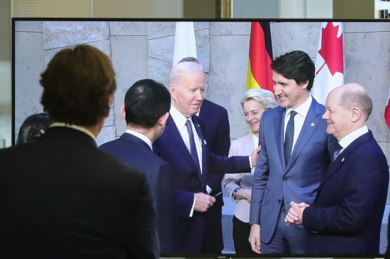 2022年3月24日，在比利時布魯塞爾的北約總部，一名男子觀看屏幕上美國總統(tǒng)拜登（右四）、歐盟委員會主席馮德萊恩（右三）、加拿大總理特魯多（右二）、德國總理朔爾茨（右一）出席七國集團(tuán)峰會合影儀式的畫面。新華社記者鄭煥松攝