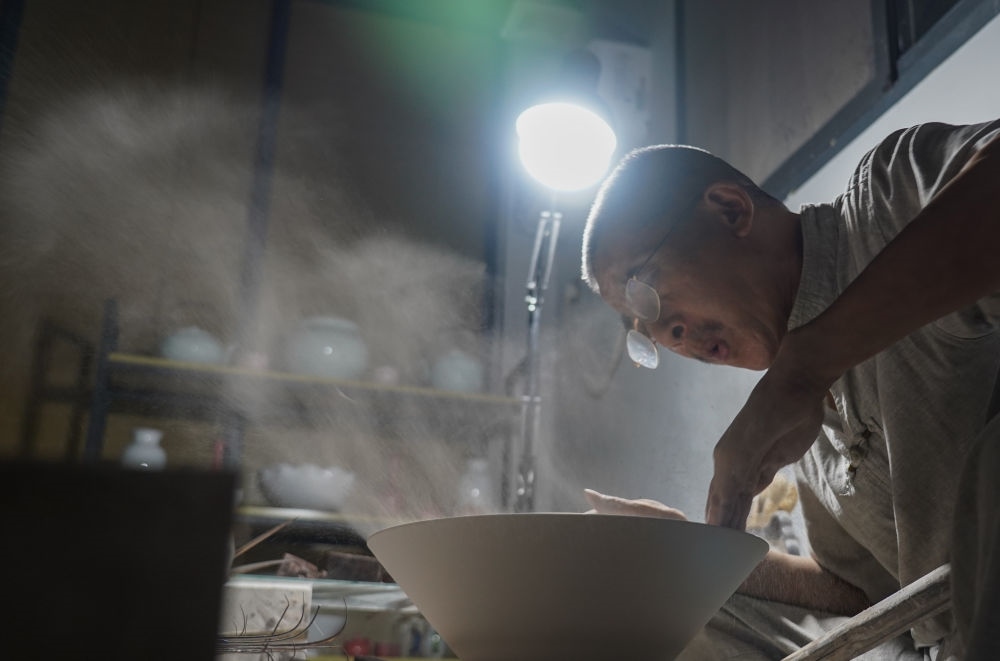 ↑ 在景德鎮(zhèn)，手工匠人吹去坯內(nèi)的泥土（2021年7月14日攝）。