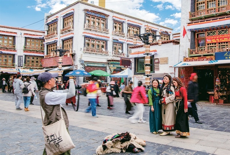 千年八廓街，見證民族團(tuán)結(jié)。2021年7月，習(xí)近平總書記來到位于西藏拉薩老城區(qū)的八廓街，感慨地說：“千年八廓街，是我們各民族建起來的八廓街。各民族文化在這里交流交往交融，我們中華民族的大家庭在這里其樂融融?！眻D為2023年6月13日，游客身著藏裝在八廓街拍照留念。 新華社記者 姜帆/攝