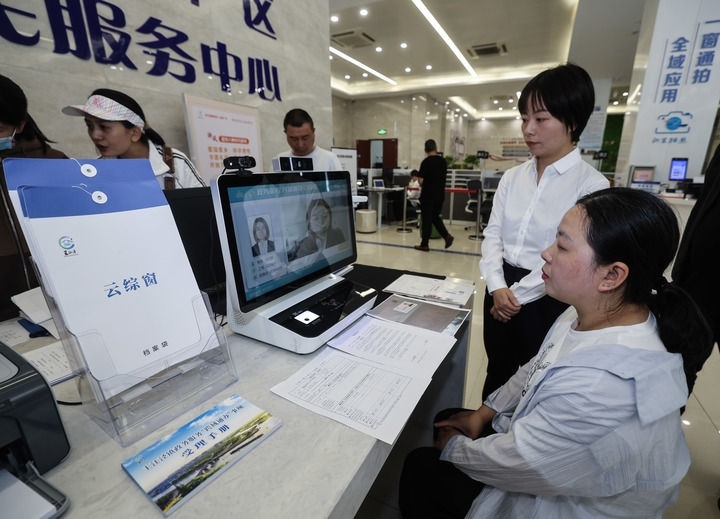 在浙江省嘉興市秀洲區(qū)王江涇鎮(zhèn)便民服務中心的“跨域通辦·云綜窗”窗口，辦理開業(yè)登記的個體工商戶（右一）通過該系統(tǒng)與江蘇省蘇州市吳江區(qū)盛澤鎮(zhèn)行政審批局工作人員視頻連線，進行身份讀取及材料線上審核（2024年5月9日攝）。新華社記者 徐昱 攝
