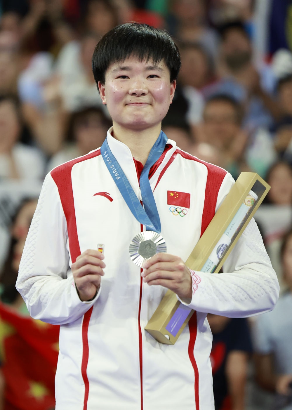 巴黎奧運(yùn)會(huì)羽毛球女子單打亞軍、中國(guó)選手何冰嬌在頒獎(jiǎng)儀式上一手握著銀牌，一手握著西班牙奧委會(huì)徽章（2024年8月5日攝）。新華社記者 任正來(lái) 攝