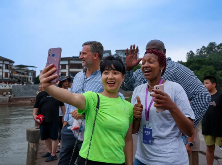 2024“一帶一路”媒體合作論壇聯(lián)合采訪調(diào)研行成員在樂(lè)山蘇稽古鎮(zhèn)與游客合影留念。本報(bào)記者 伊霄攝