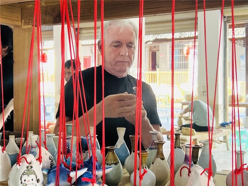 鄉(xiāng)愁如同一根根紅線，將游子與故鄉(xiāng)永遠地牽連到一起?；逄账囄幕瘎?chuàng)意一條街的母氏陶藝館內，紅線吊著陶瓶，思緒游走萬里。摩爾多瓦“信息標簽”通訊社社長亞歷山大·塔納斯端詳著館內展示的陶藝作品，并挑選出心儀的小擺件帶回摩爾多瓦，也帶走花茂村的“鄉(xiāng)愁”。（張亞欣攝）